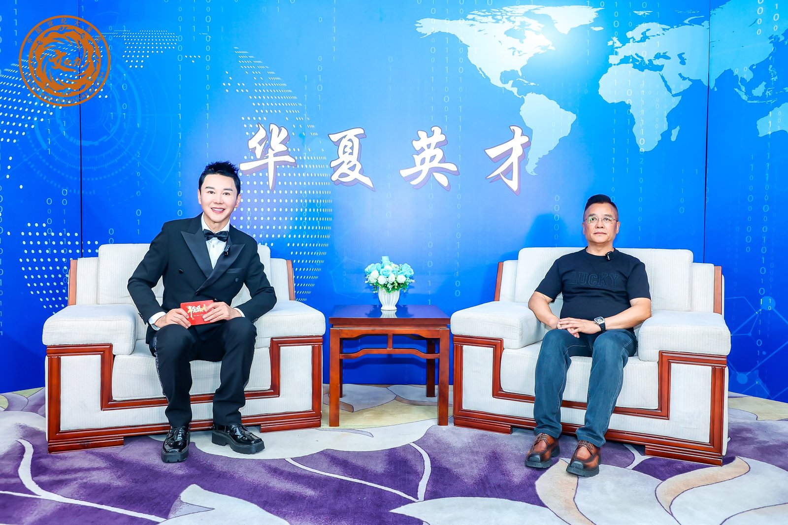 电视访谈现场照：背景板「华夏英才」，两人坐谈