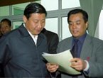 两人在室内交谈，一人手持材料